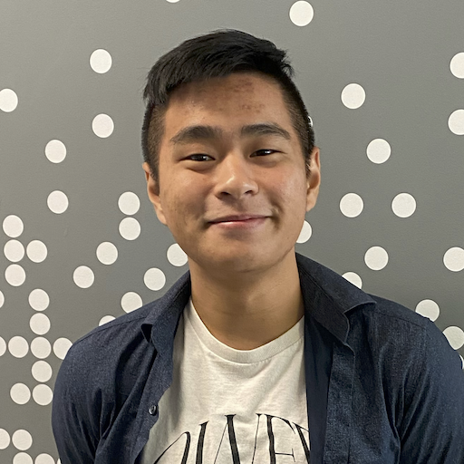 Matt Wang, an Asian man, smiles directly at us, with short black hair. He is against a gray background with white spots, wearing a white t-shirt with a blue jacket open.