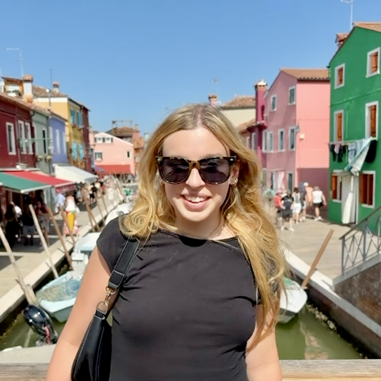 A photo of Evelyn, a 12X TA, smiling in sunglasses in front of a street with colorful houses..