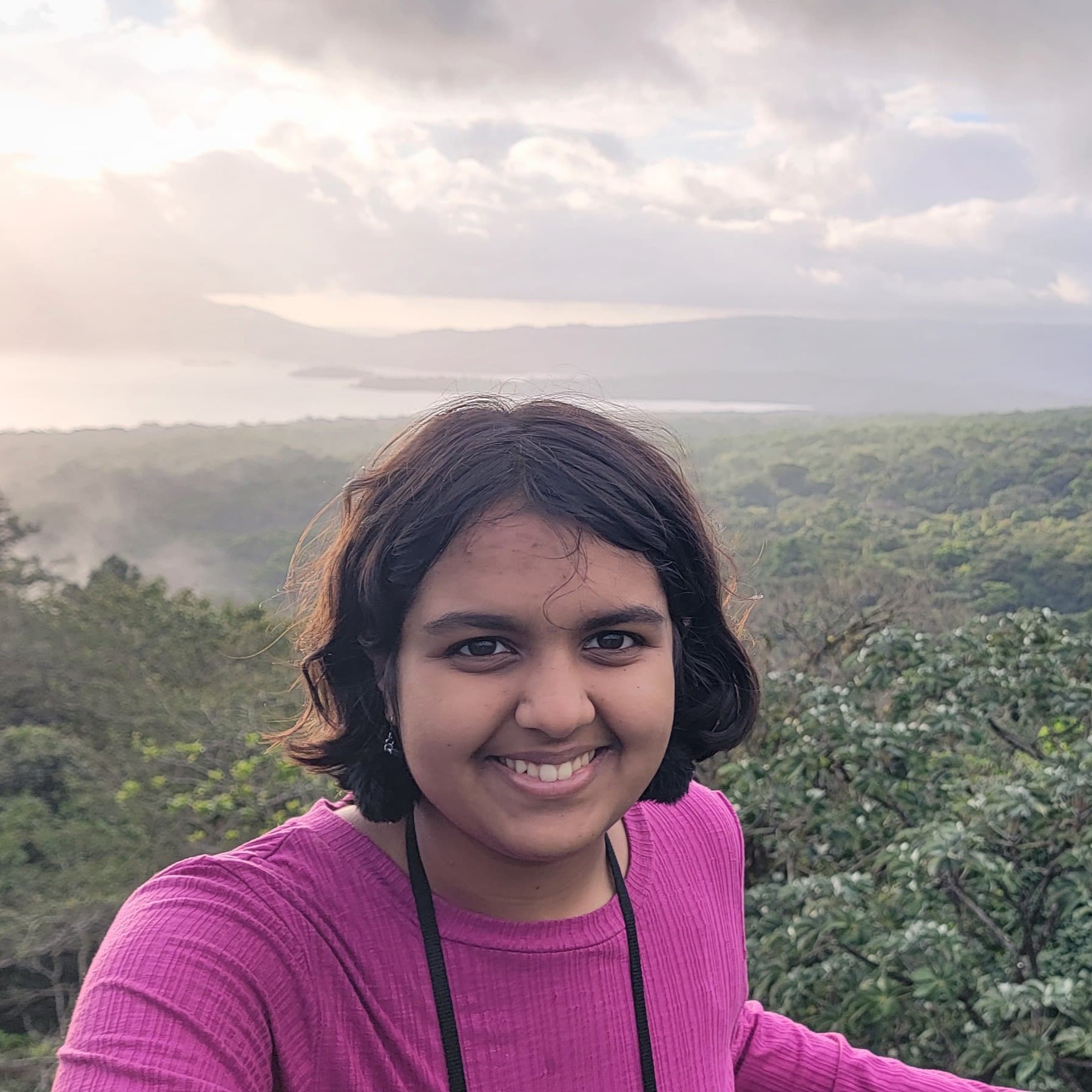 Navya Jain, a South Asian female, smiling in front of an overhead view of a rainforest.