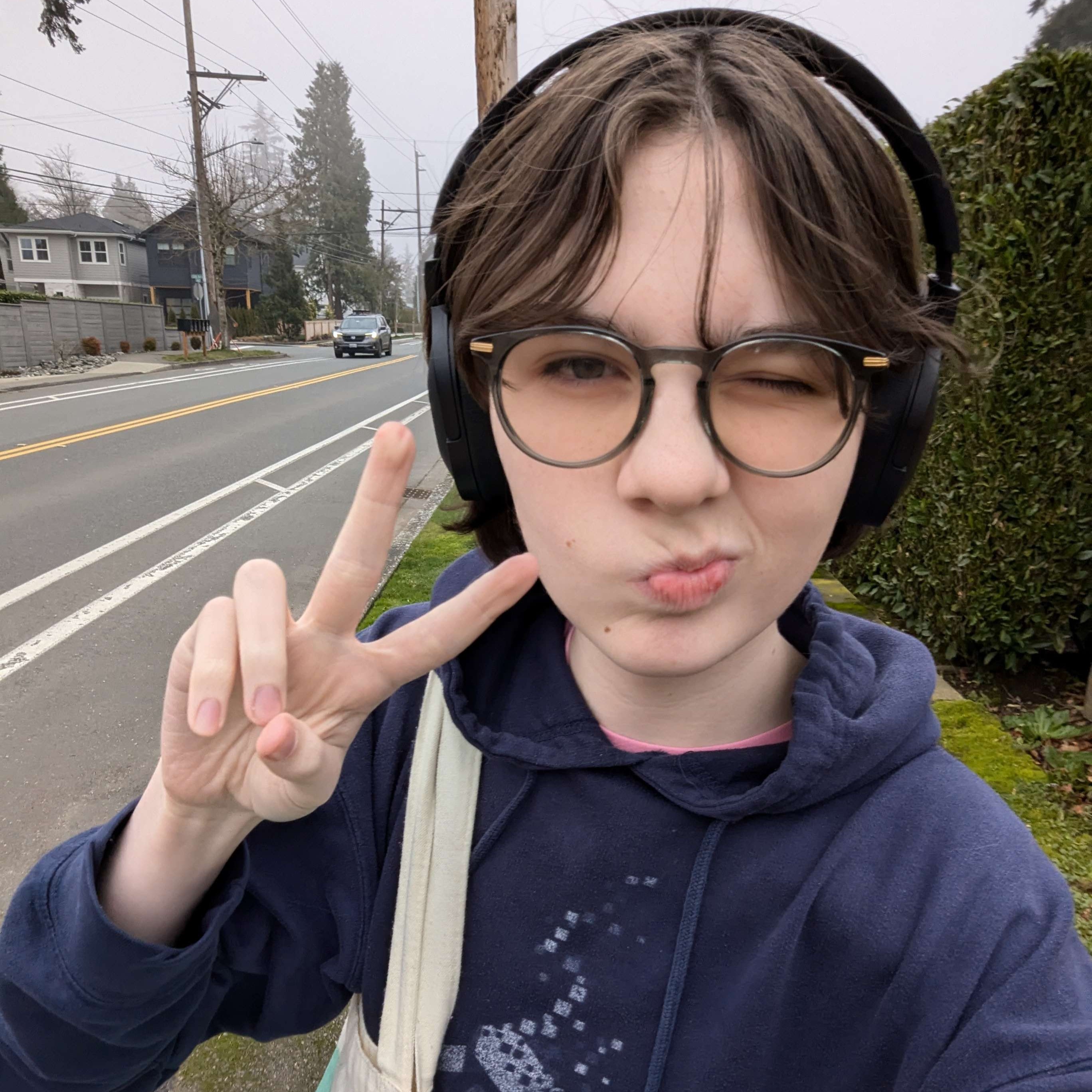 Sarah is winking at the camera and making a peace sign next to a bush.