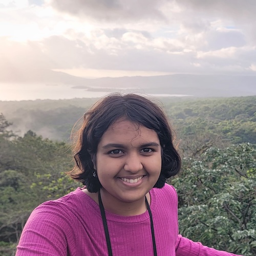 Navya Jain, a South Asian female, smiling in front of an overhead view of a rainforest.