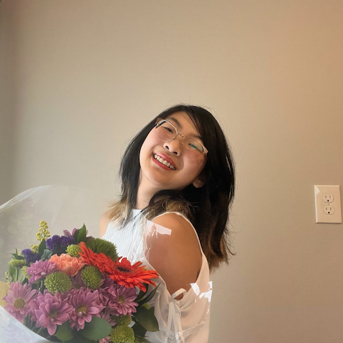 Jessica Luo, an Asian woman with black hair and glasses, holding a bouquet and smiling at the camera.