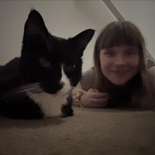 young girl with bangs taking selfie with tuxedo cat on floor