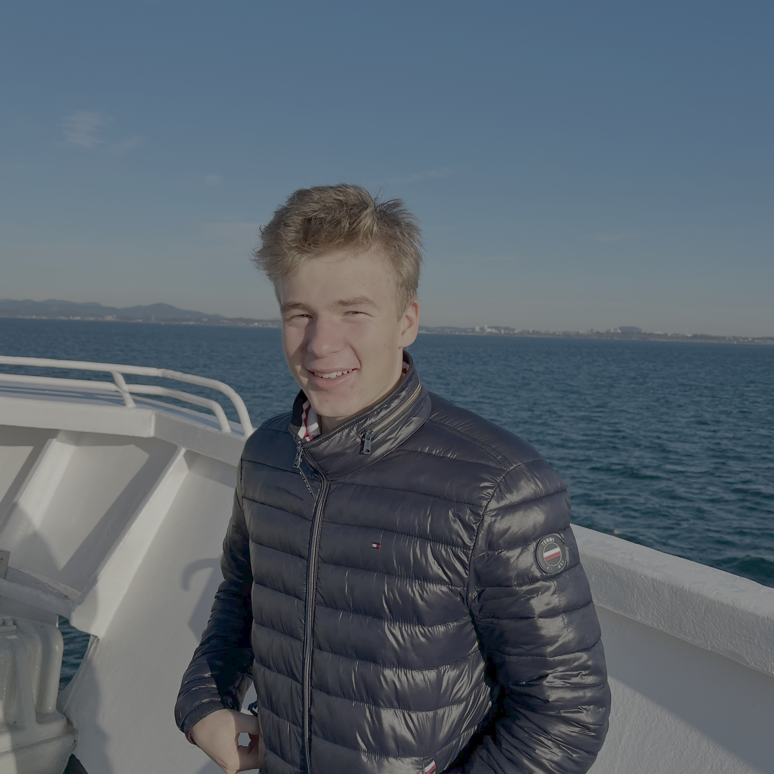 Paul, smiling, standing on a ferry traveling through the windy ocean.