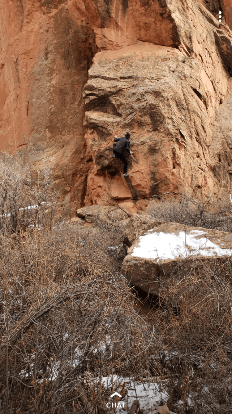 person climbing red rock from far away