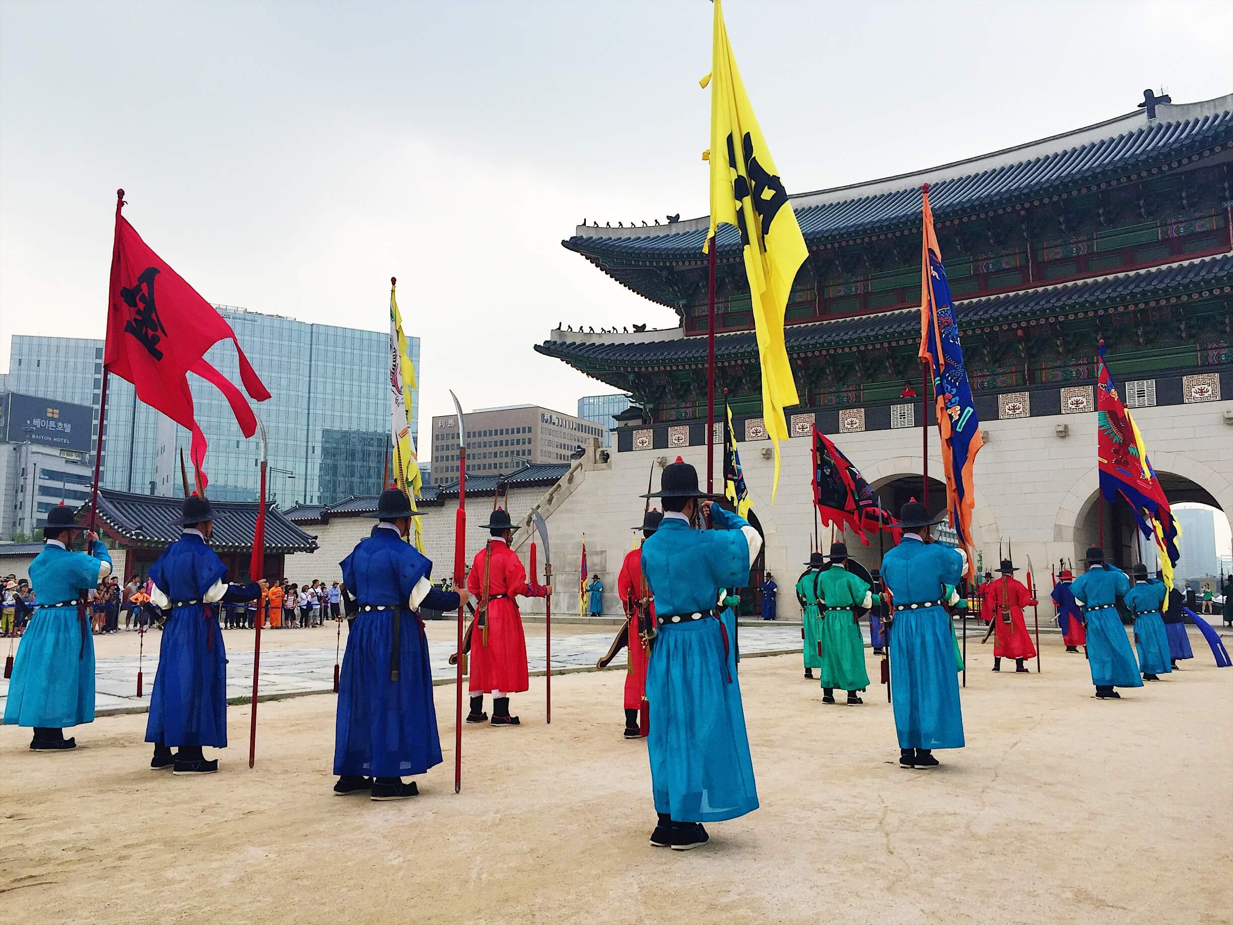 Outside Gyeongbokgung
              Palace, there are guards wearing colored clothing and holding
              up colored flags.