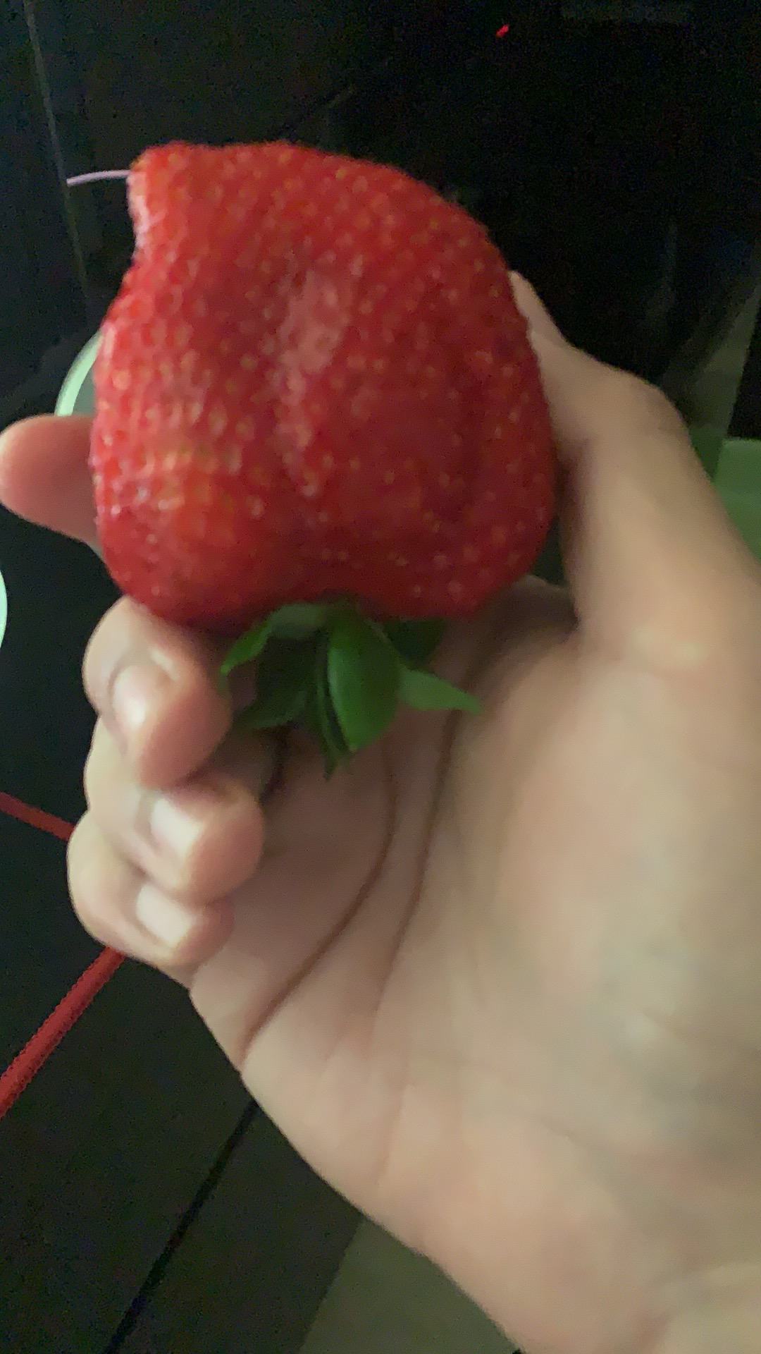 Holding a huge strawberry with my right hand.