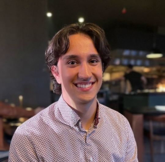A profile picture of Ari sitting in a restaurant and smiling at the camera