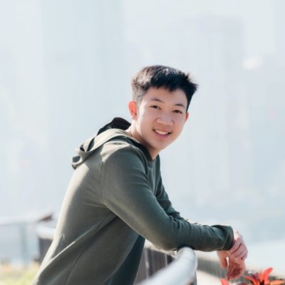 Hansel leaning on a railing and smiling, with a hazy city skyline behind him.