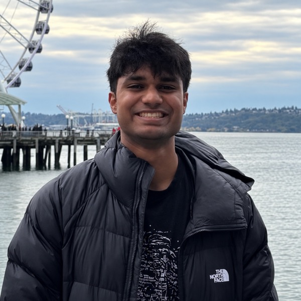 Naren smiling by the waterfront with the Ferris wheel and water behind him.