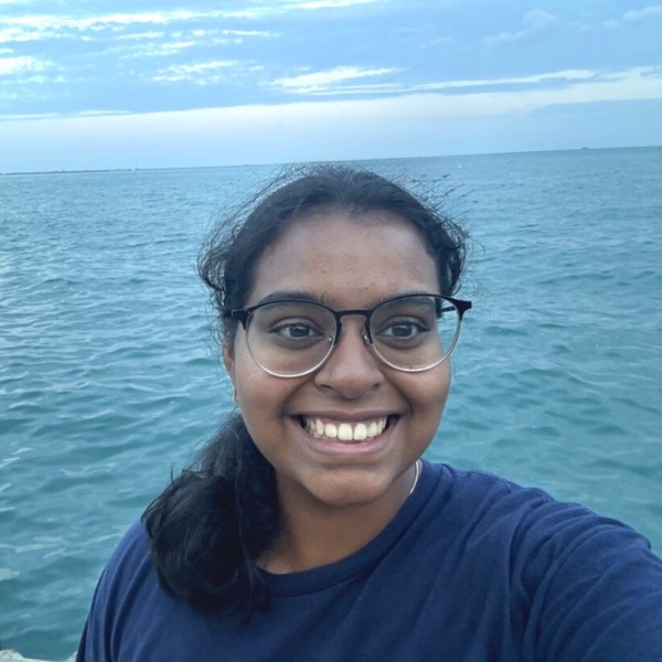 A picture of Pratika smiling at the camera with the ocean behind