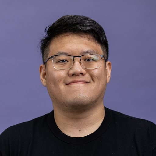 Yihong in glasses and a black T-shirt, smiling against a purple backdrop.