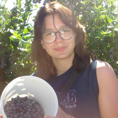 Emily holding a bucket of blueberries and smiling at the camera.