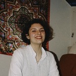 Headshot of Alena, taken indoors in front of a patterned, weaved wall decor.