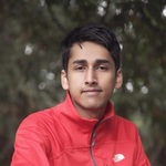 Portrait of Rahul, wearing a red jacket, in front of a blurred background of dark green trees.