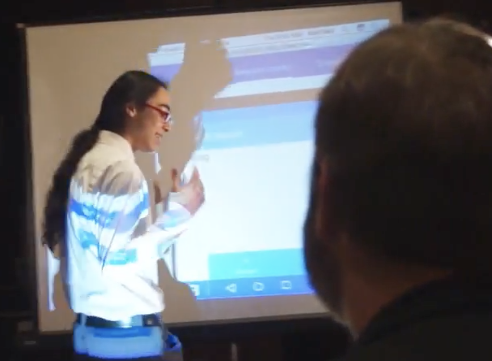 :img Headshot of Kavi walking in front of an android demo, 70%