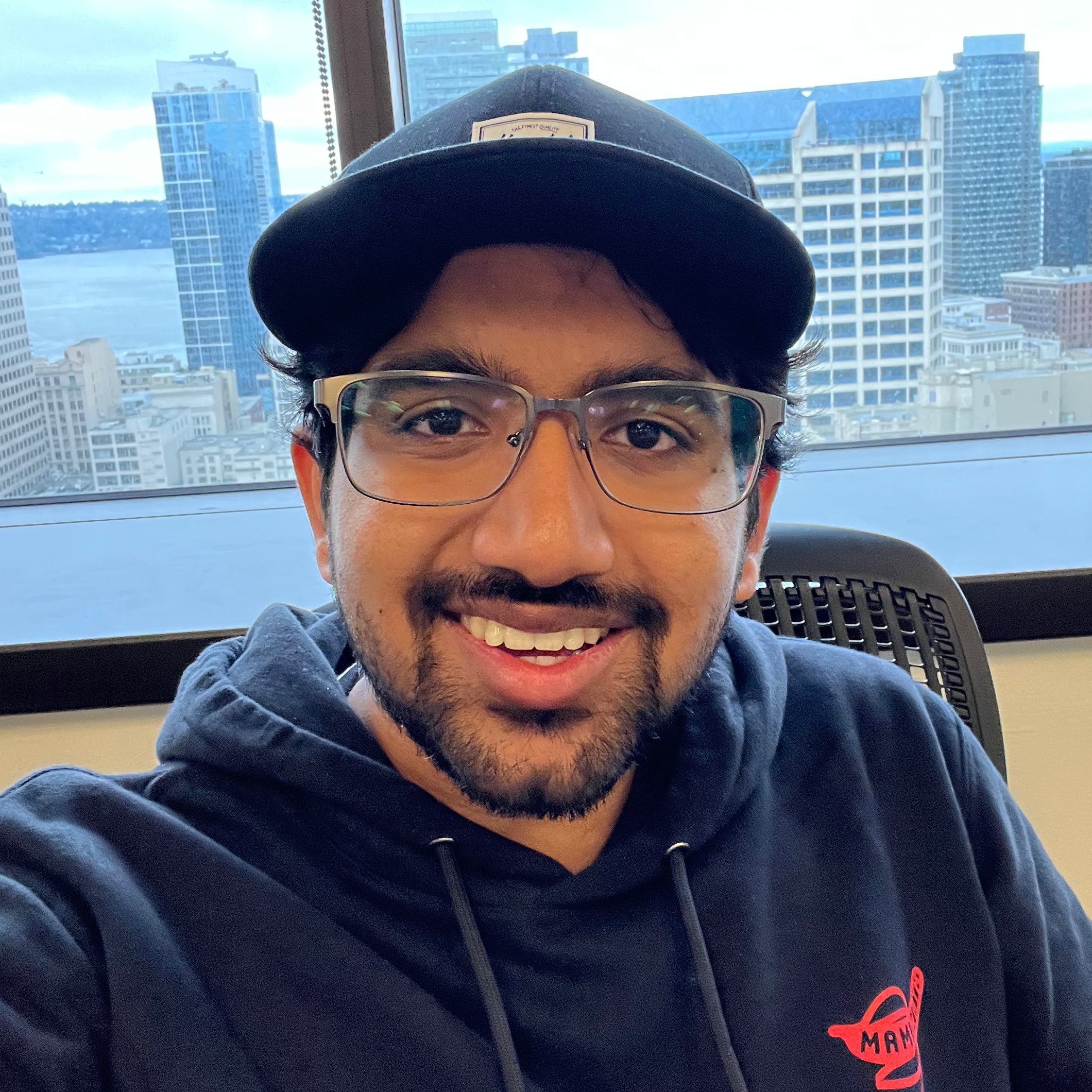 A headshot of Amal Jacob looking at the camera. He is a brown man with a 
    beard and is wearing a black sweatshirt and black hat.