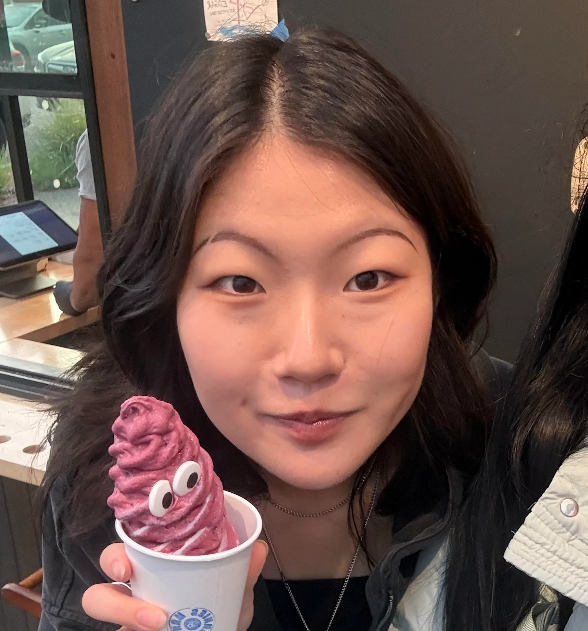 Girl smiling looking into camera holding a purple icecream with googly eyes