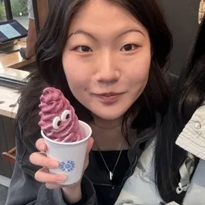 Girl smiling looking into camera holding a purple icecream with googly eyes