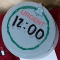 A paper prototype watch face showing the time, and green ring with the MindMii logo, and bold text saying URGENT.
