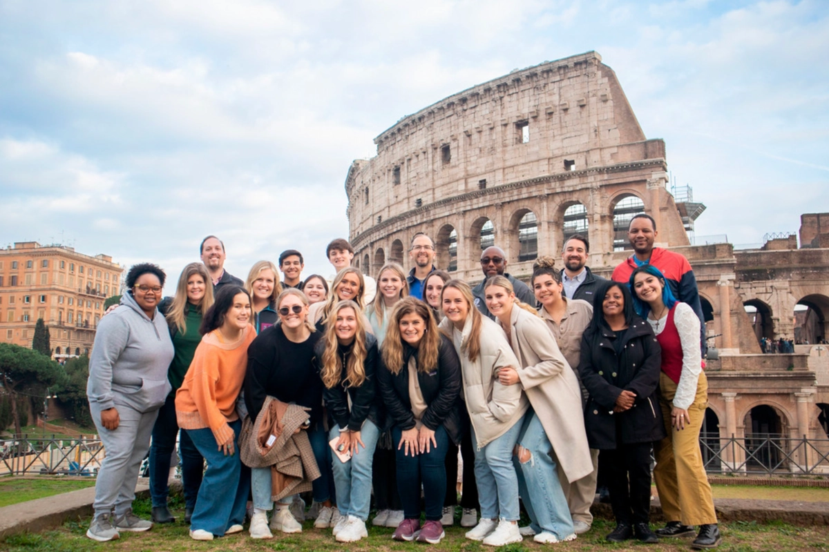 A large group of friends pose for a photo by the Colosseum