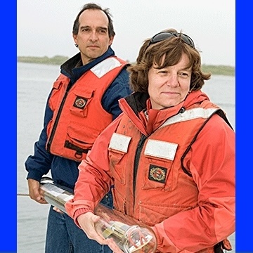 Amy Bower & colleague wearing life jackets in front of water, holding equipment