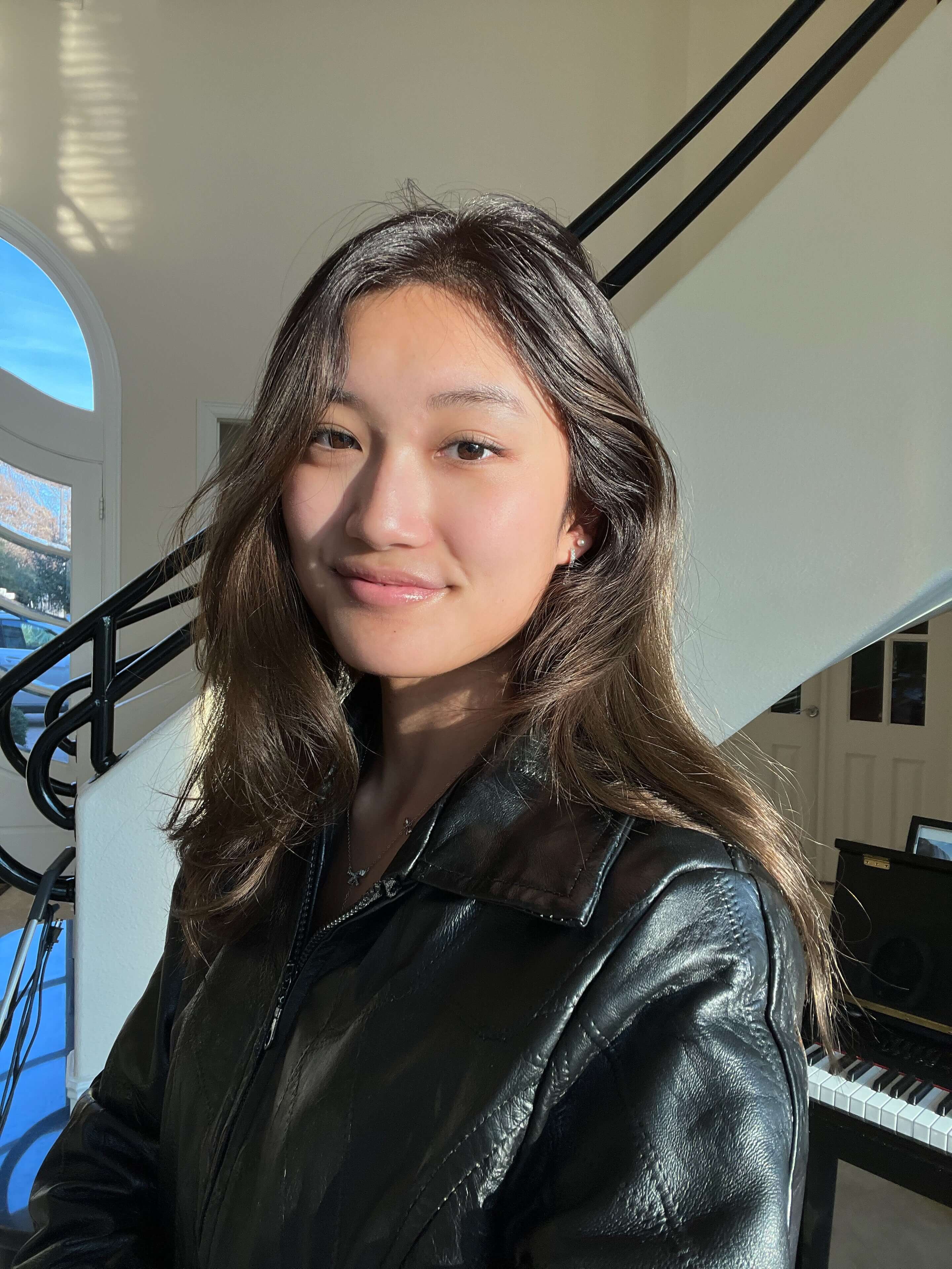 A picture of a young adult female with long dark brown hair who is wearing a black leather jacket and smiling