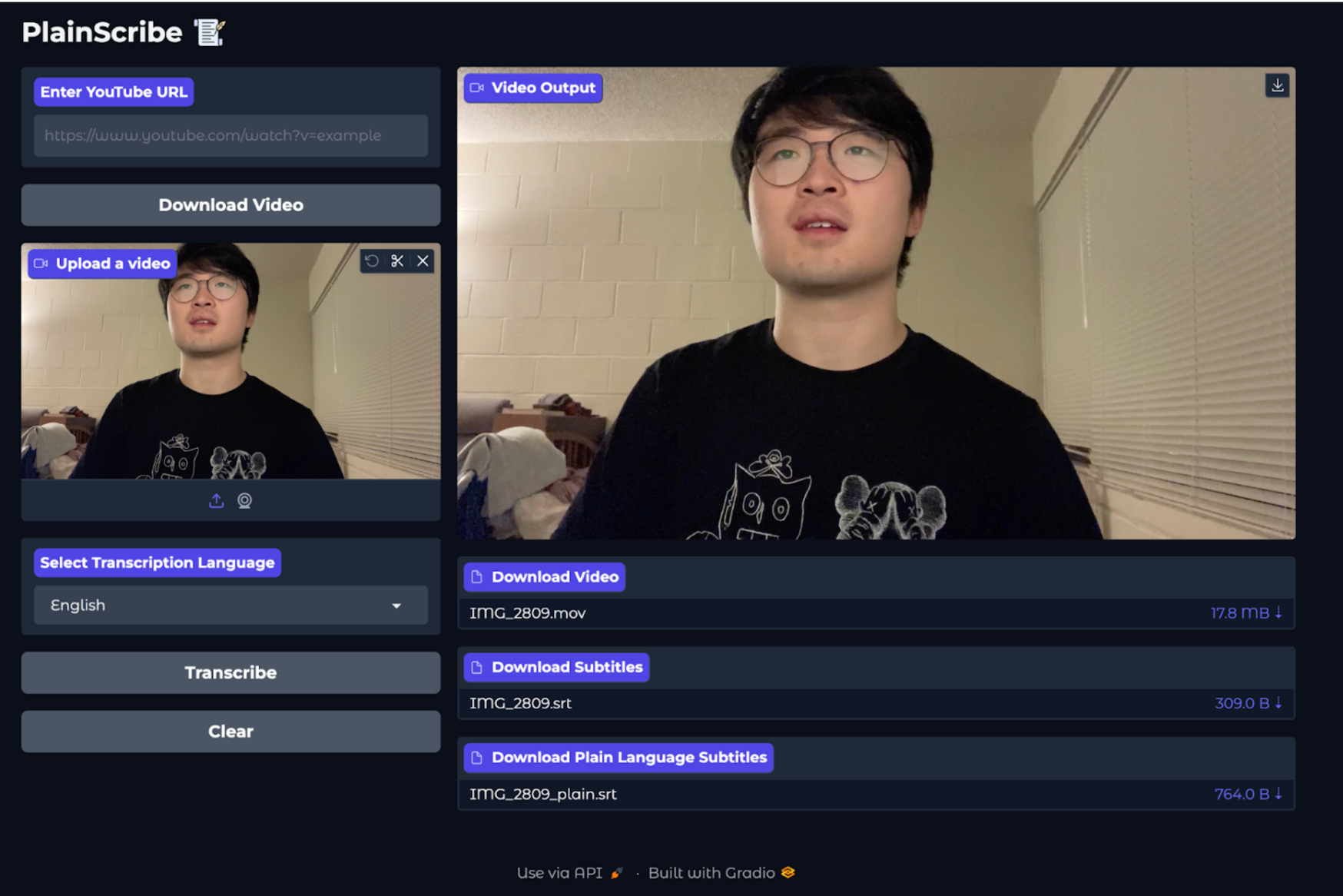 Screenshot of PlainScribe web app user interface. On the left side of the interface, there is a box for entering YouTube video URL with Download Video button below it. Below the button is a thumbnail of a user’s uploaded video. Under the uploaded video thumbnail is dropdown menu for selecting transcription language. Below the dropdown is the Transcribe button followed by a Clear button. On the right side, there is an image of the video output. Under the video output image is an option to download the video followed by an option to download the plaintext transcript of the video.