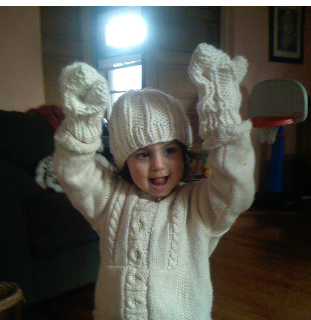 :img A picture of Jen's child 3 at age wearing a white knit sweater; knit mittens and a knit hat. The mittens are a bit too large and he has his hands raised in the air to show them off and a smile on his face., 100%, width