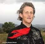 Head shot of Temple Grandin out in nature with her red tie blowing in the wind